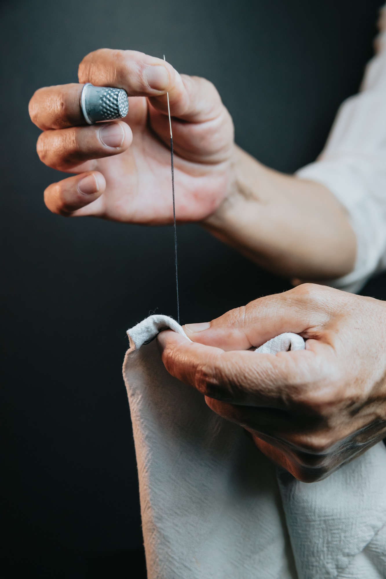 Workshop hands threading needle over linen